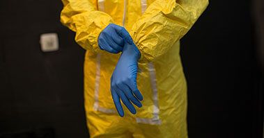 A worker in a hazmat suit putting on some gloves
